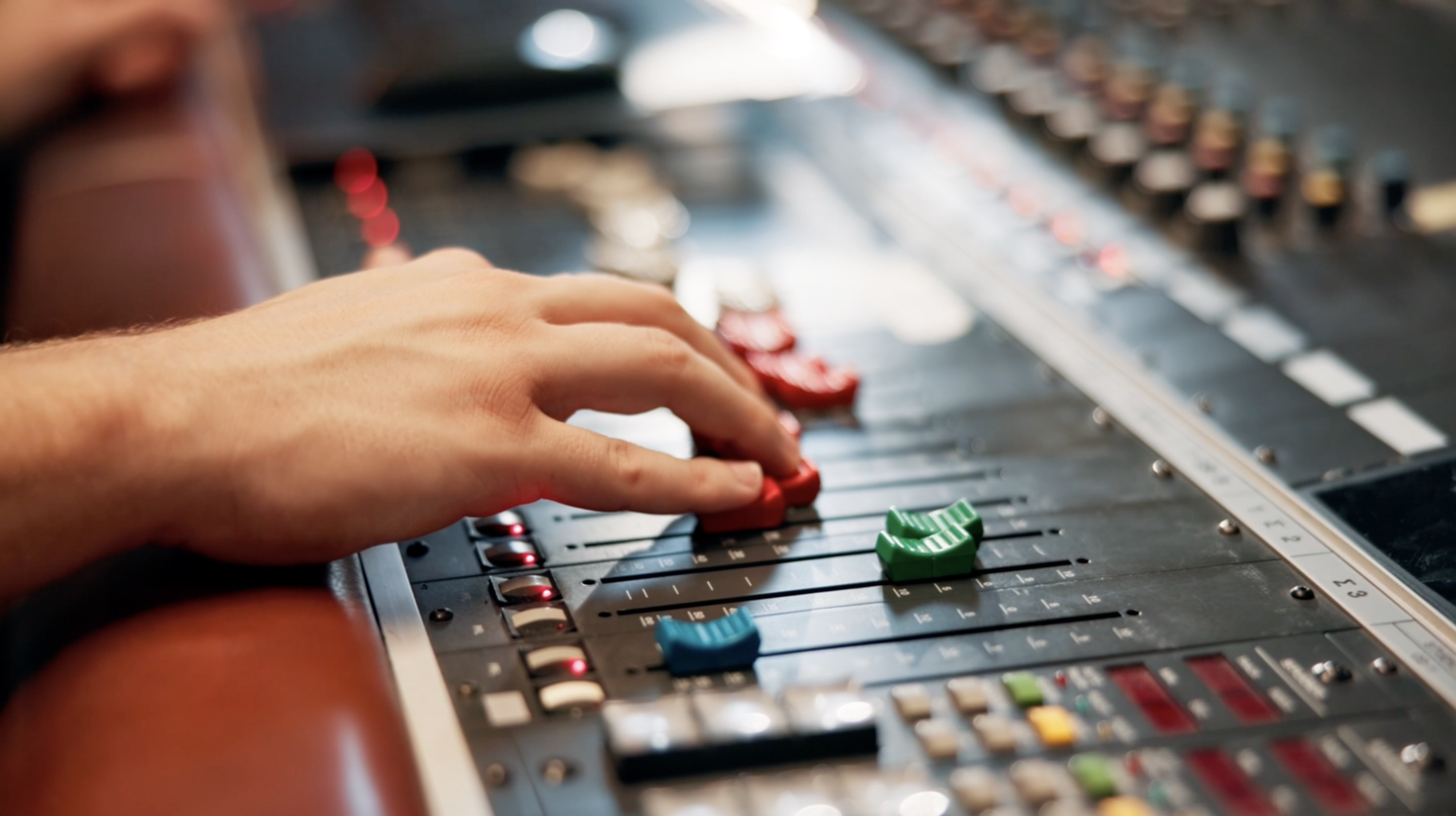 A hand adjusts sliders on a professional audio mixing console.