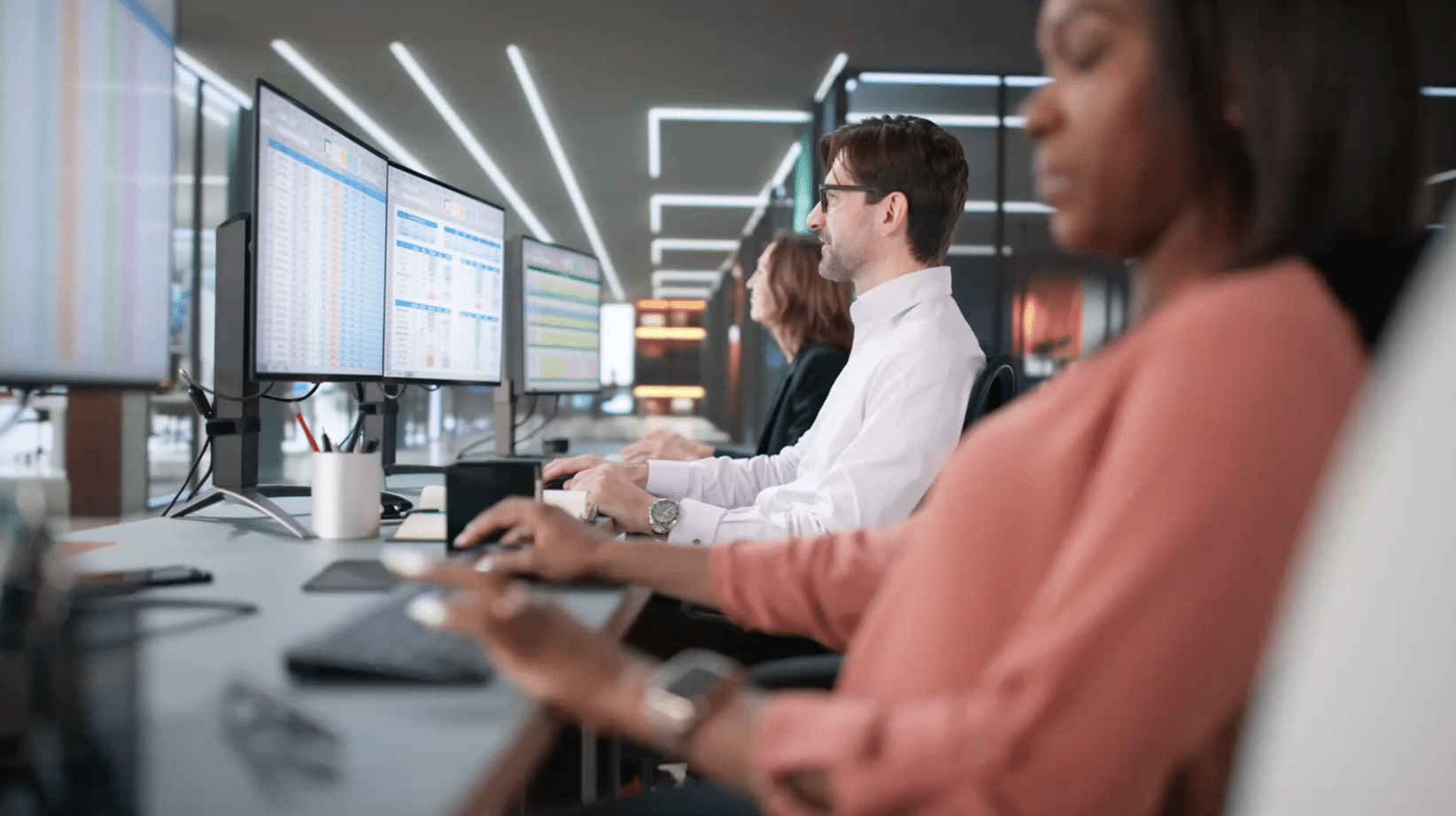 People are working at desks with multiple computer monitors displaying data in a modern office setting.