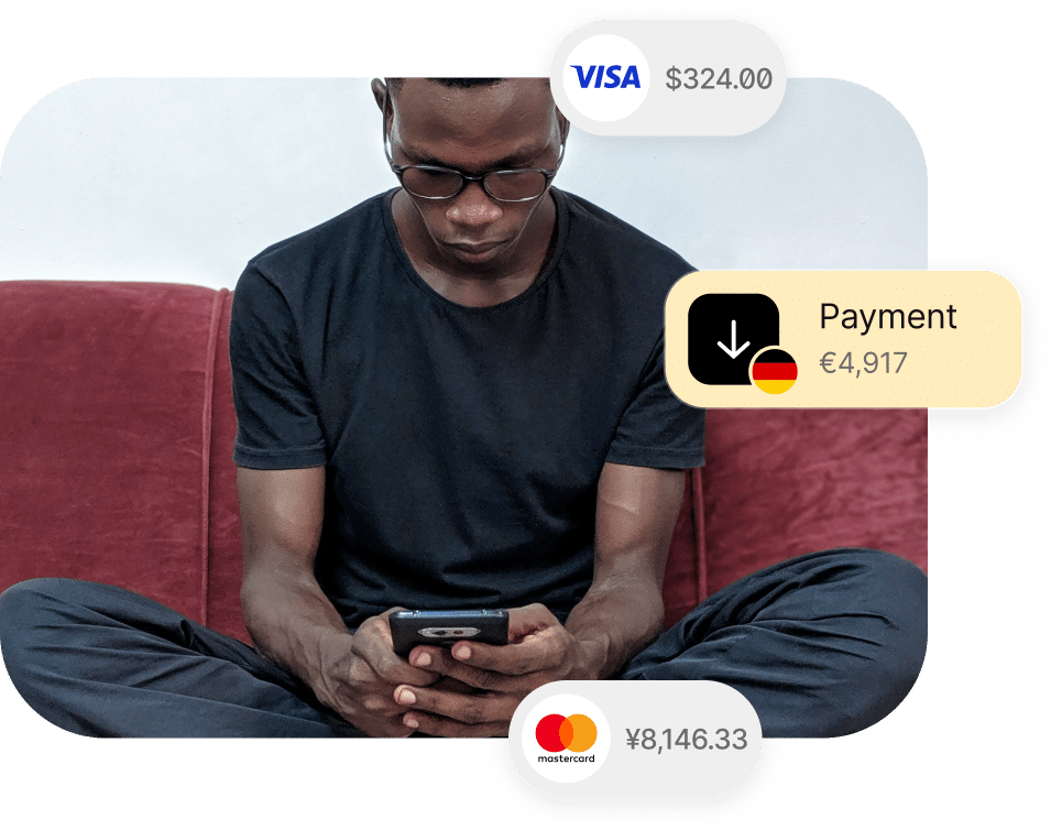 A person in a black shirt and glasses is using a smartphone while sitting cross-legged on a red couch. Payment icons with amounts in different currencies appear around them.