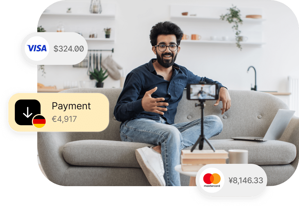 A man sits on a couch with a laptop and smartphone on a tripod. Payment notifications are displayed around him, showing amounts in USD, EUR, and JPY with logos for Visa, Mastercard, and a download symbol.