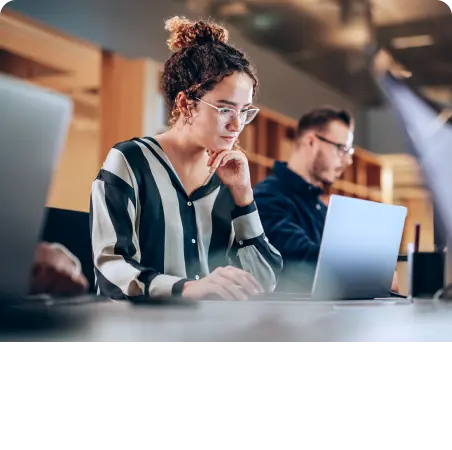A group of people engrossed in their laptops, diligently working in a bustling office environment.