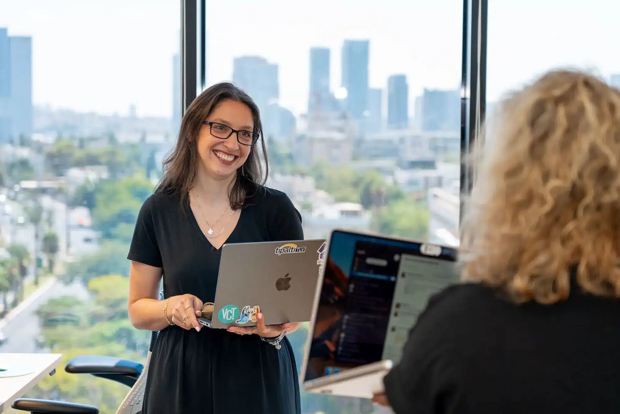 A woman holding a laptop in front of a window.